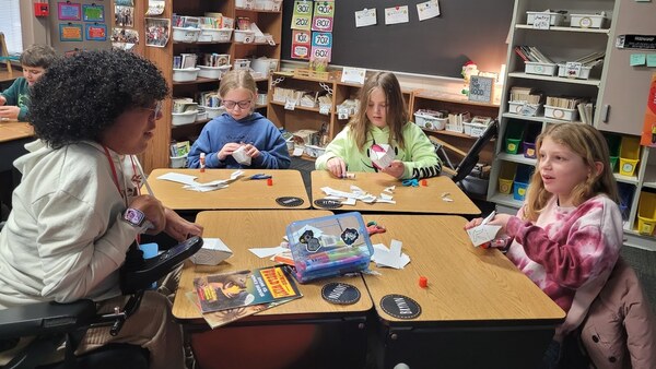 Students sitting around a table crafting dreidels out of paper.