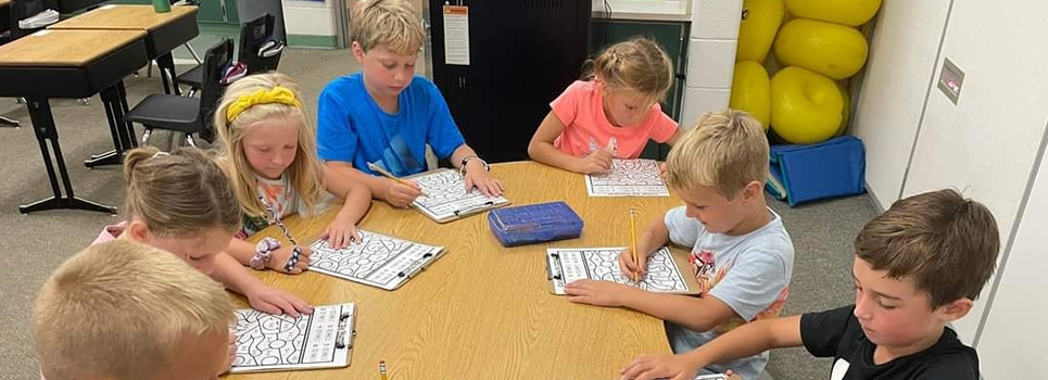 Elementary students sit around a table working on math skills.